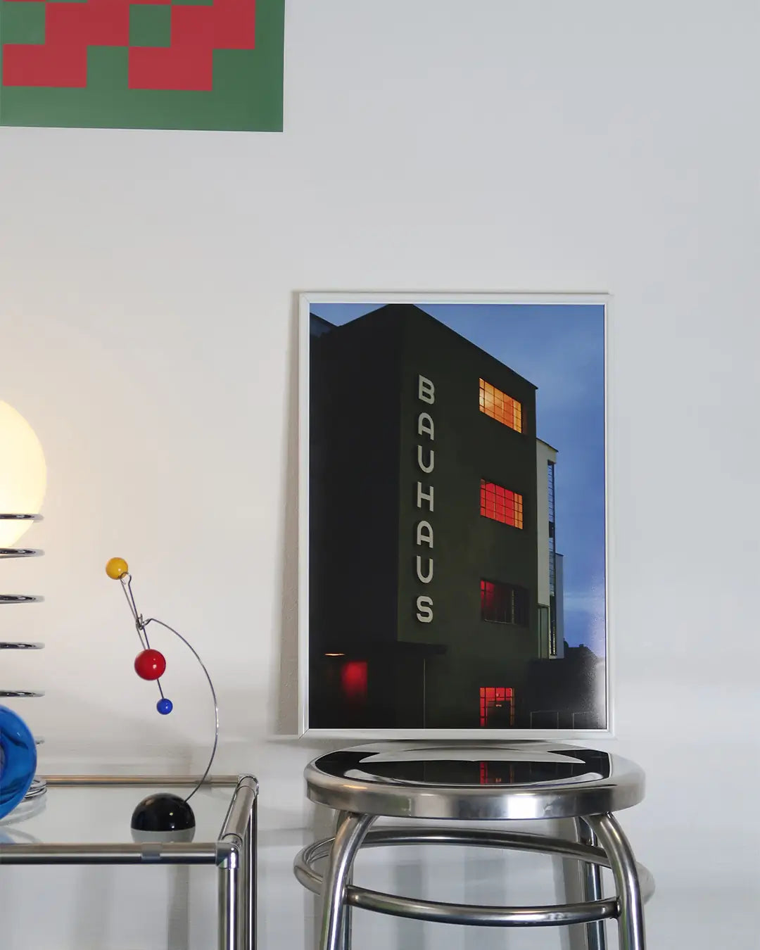 スツールの上に立てかけられたホワイトフレームのバウハウス建築写真ポスター。機能美あふれるモダンな建築デザインが映えるアートポスター。