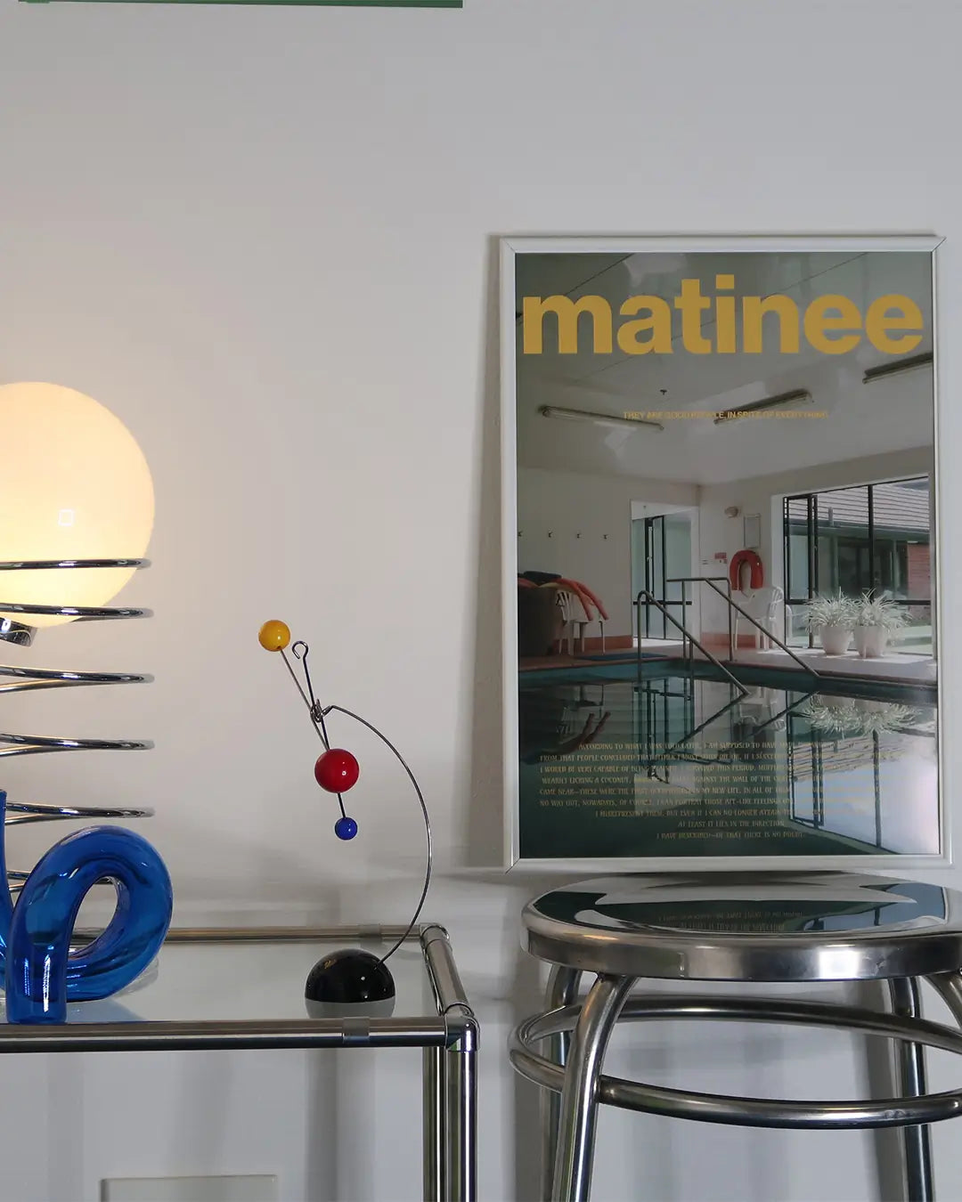 スツールの上に立てかけられたホワイトフレームの「Matinee」ポスター。落ち着いた色彩が空間に映えるモダンアートポスター。